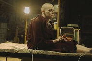 Michelle (Emma Stone) sitting on a cot with a shaved head in Bugonia (2025).
