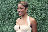 Keke Palmer smiling and posing in front of foliage.